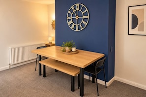 A dining area with a wooden table, black chairs, a wall clock, a potted plant, and a framed picture. - The Cozy Gateshead Escape (Tyne and Wear)