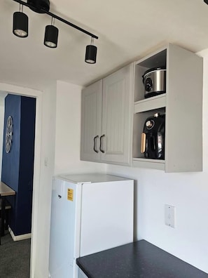 A compact kitchen with a white refrigerator, a built-in oven, and a coffee maker on the upper shelf. - The Cozy Gateshead Escape (Tyne and Wear)