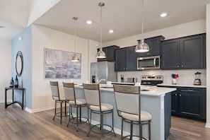 A modern kitchen with dark cabinetry, a central island with bar stools, and pendant lighting. - NEW Disney Clubhouse & Themed BR I Near Clubhouse (Davenport)