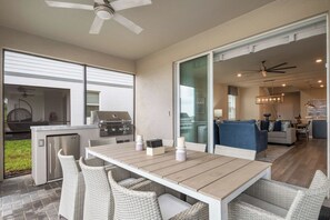 Une terrasse avec une table à manger, des chaises, un barbecue et un ventilateur de plafond.