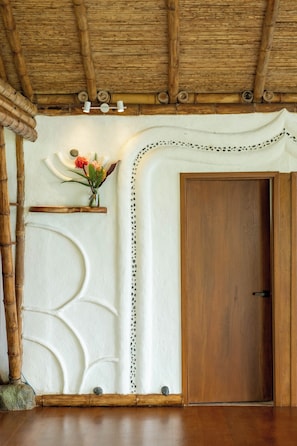 Una habitación con una puerta de madera, una pared con un diseño blanco decorativo y una estantería con flores.