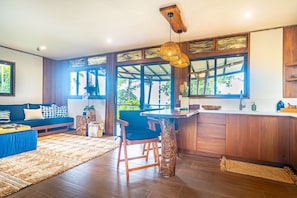 Una cocina moderna con encimera de madera, un comedor con sofá azul y grandes ventanales con vistas a zonas verdes.