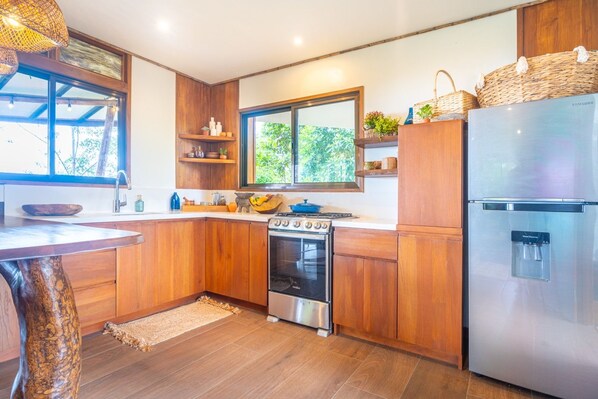 A modern kitchen with wooden cabinets, a stainless steel stove, and a refrigerator. - Earth Home with Waterfall Jungle View above Uvita Beach with River, Sauna, Yoga (San Luis)