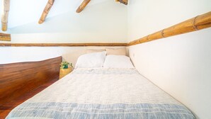 Een slaapkamer met een houten hoofdbord, een bed met een wit- en blauw gestreept dekbedovertrek en een kleine plant op het nachtkastje.