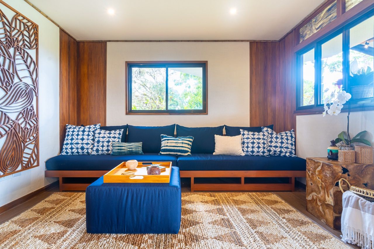 Una sala de estar moderna con un sofá azul oscuro, cojines estampados, una mesa de centro de madera y un ventanal con vistas a zonas verdes.