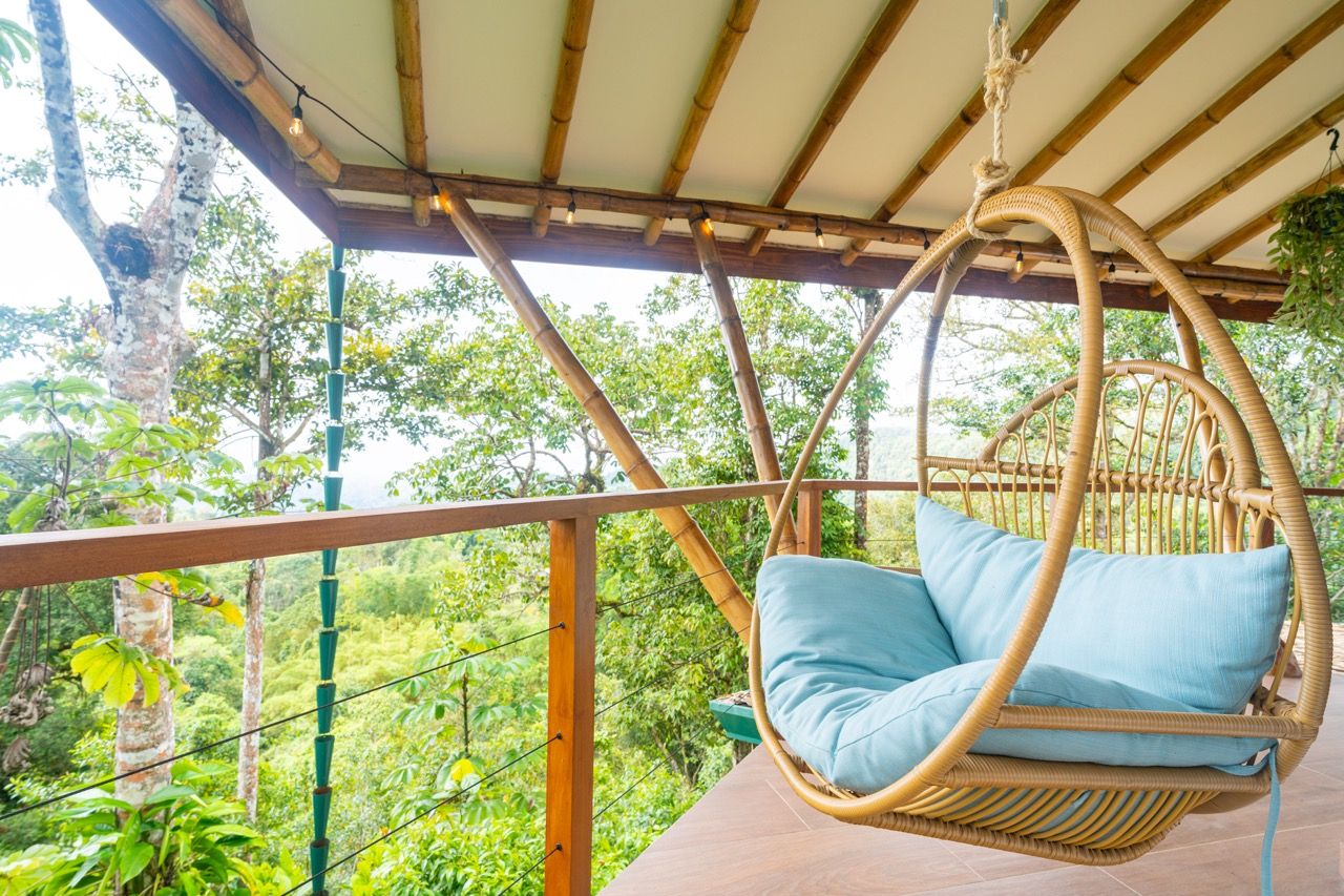 A wicker hanging chair with cushions, a wooden railing, and a view of a lush green landscape.