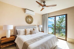 A bedroom with a large bed, a ceiling fan, an air conditioning unit, a decorative wall piece, and a view of the ocean through a large window. - Artila Isla Mujeres: Your Sanctuary of Coastal Sophistication (Isla Mujeres)