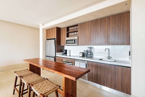 A modern kitchen with wooden cabinets, a stainless steel refrigerator, a microwave, a sink, and a wooden dining table with stools. - Artila Isla Mujeres: Your Sanctuary of Coastal Sophistication (Isla Mujeres)