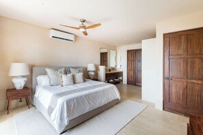 Ein Schlafzimmer mit einem großen Bett, einem Deckenventilator, einer Klimaanlage, Holzmöbeln und einer Holztür.