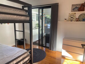 A room with a bunk bed, a desk, a chair, a small rug, and a sliding glass door leading to an outdoor area. - perfect position, well maintained home with added comforts for a luxurious stay (Sandgate)