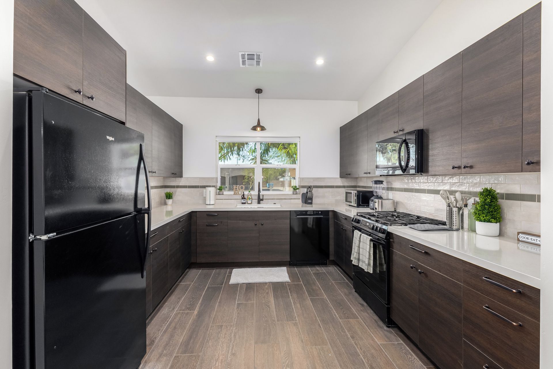 A modern kitchen with dark wood cabinets, a black refrigerator, a microwave, and a stove.