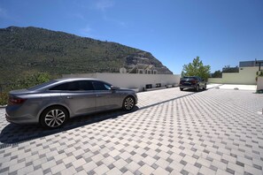 A parking area with two cars, a hilly landscape in the background, and a building with a flat roof. - Luxury Villa Mandy with Heated Pool, Jacuzzi & Sauna (Žrnovnica)