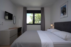 Een hotelkamer met een bed, bureau, stoel, televisie, raam met gordijnen en een wandlamp.