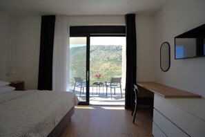 A hotel room with a bed, a desk, a chair, and a view of a mountainous landscape through a sliding glass door. - Luxury Villa Mandy with Heated Pool, Jacuzzi & Sauna (Žrnovnica)