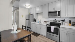 A modern kitchen with white cabinets, stainless steel appliances, and a wooden dining table. - 2BR Walk to Main St · Laundry + Parking · Pets OK (Gilbert)