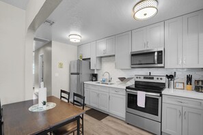 Una cocina moderna con armarios blancos, electrodomésticos de acero inoxidable y una mesa de comedor de madera.