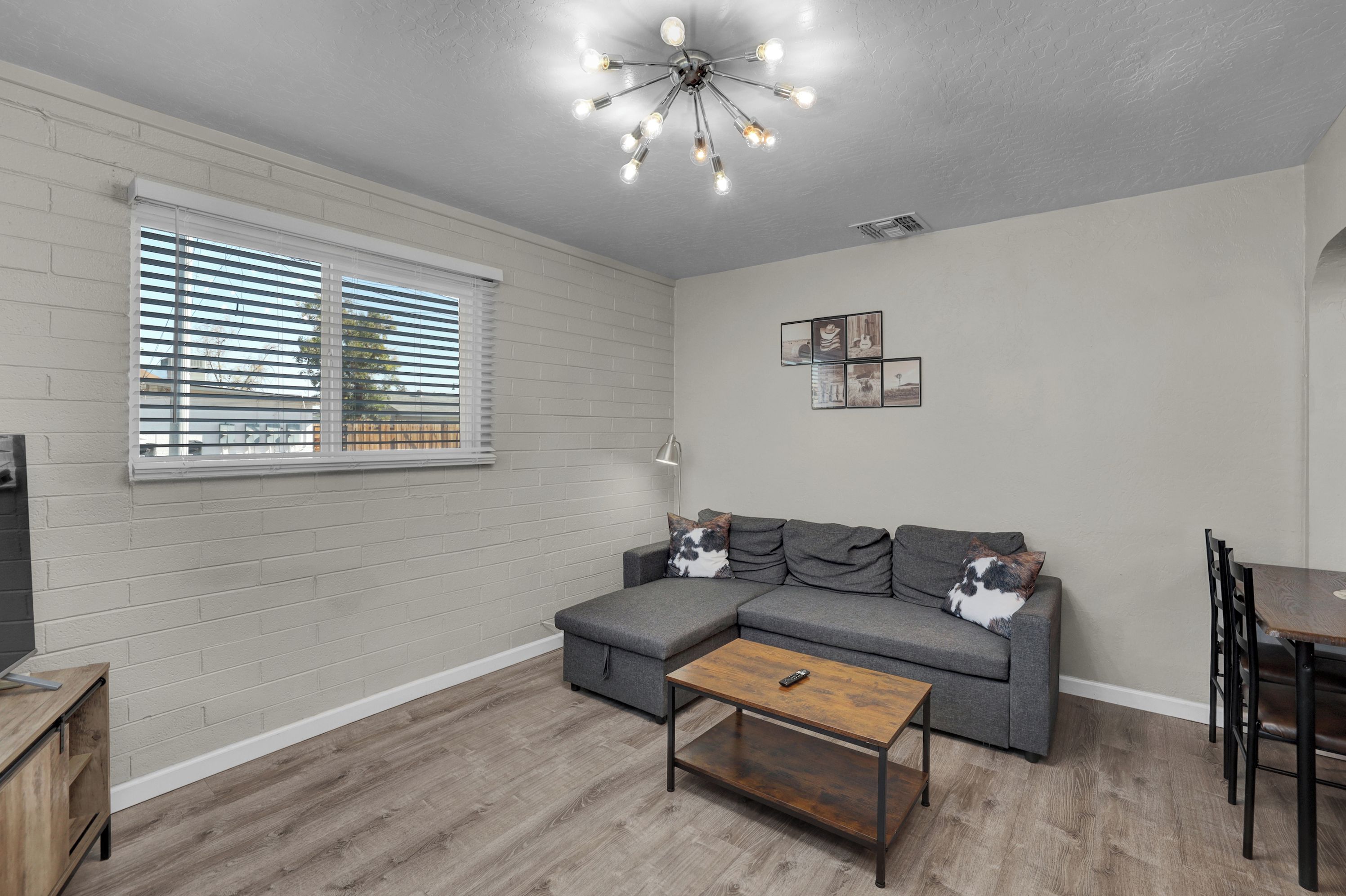 A living room with a sectional sofa, a coffee table, a dining table, and a ceiling light fixture.