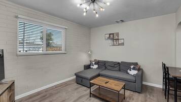 A living room with a sectional sofa, a coffee table, a dining table, and a ceiling light fixture.