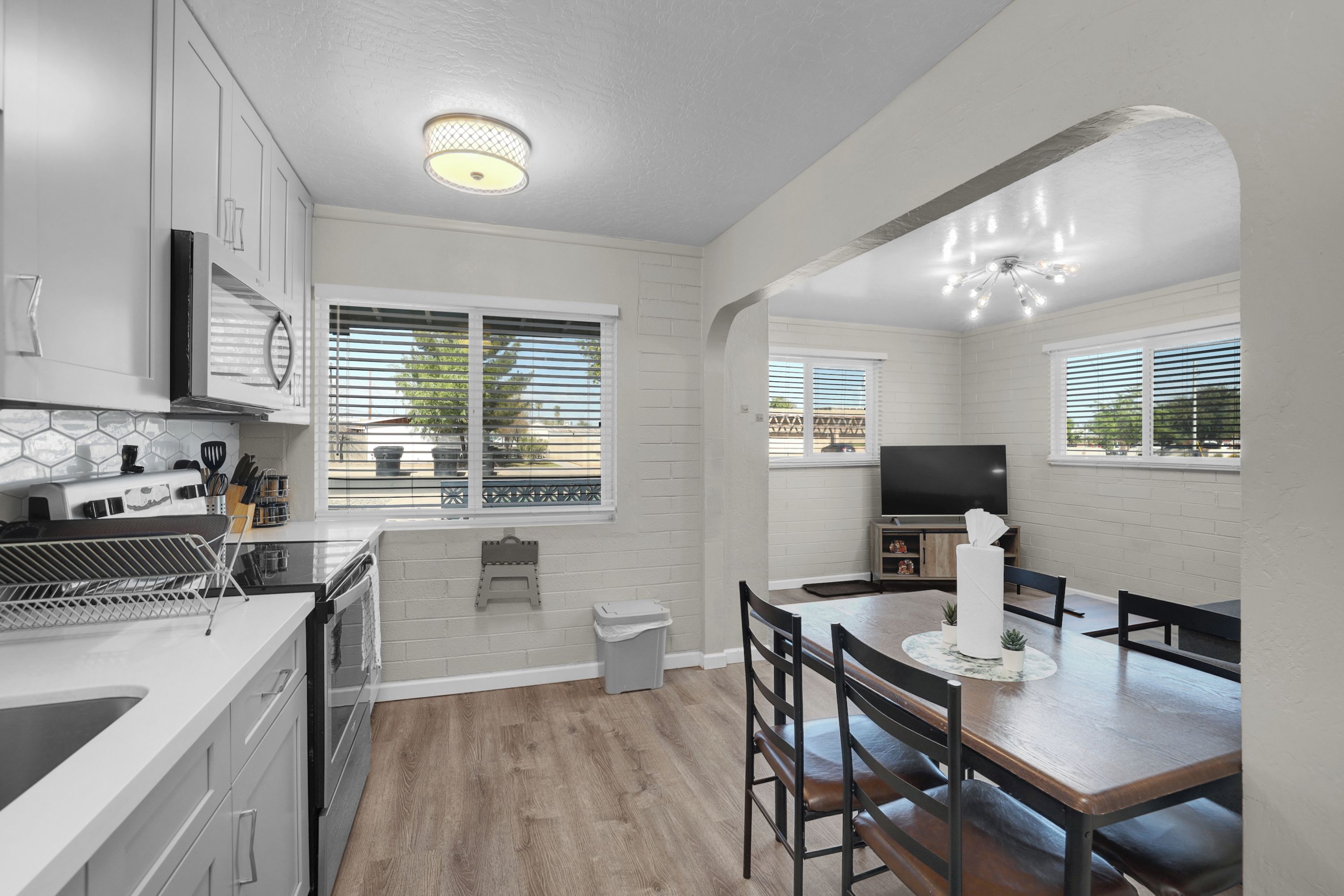 Una cocina moderna con armarios blancos, estufa integrada y comedor con mesa y sillas de madera.