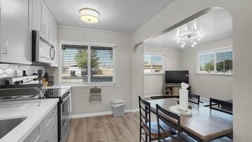 Una cocina moderna con armarios blancos, estufa integrada y comedor con mesa y sillas de madera.