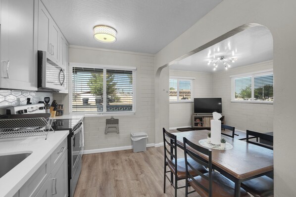 Una cocina moderna con armarios blancos, estufa integrada y comedor con mesa y sillas de madera.