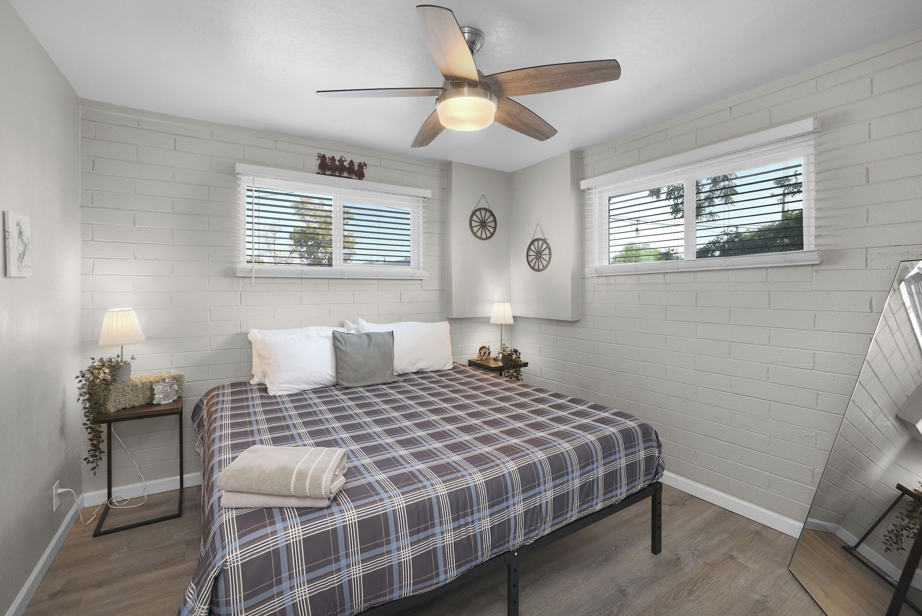 A bedroom with a bed, two bedside tables, a ceiling fan, and two windows with blinds.