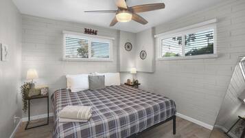 A bedroom with a bed, two bedside tables, a ceiling fan, and two windows with blinds.