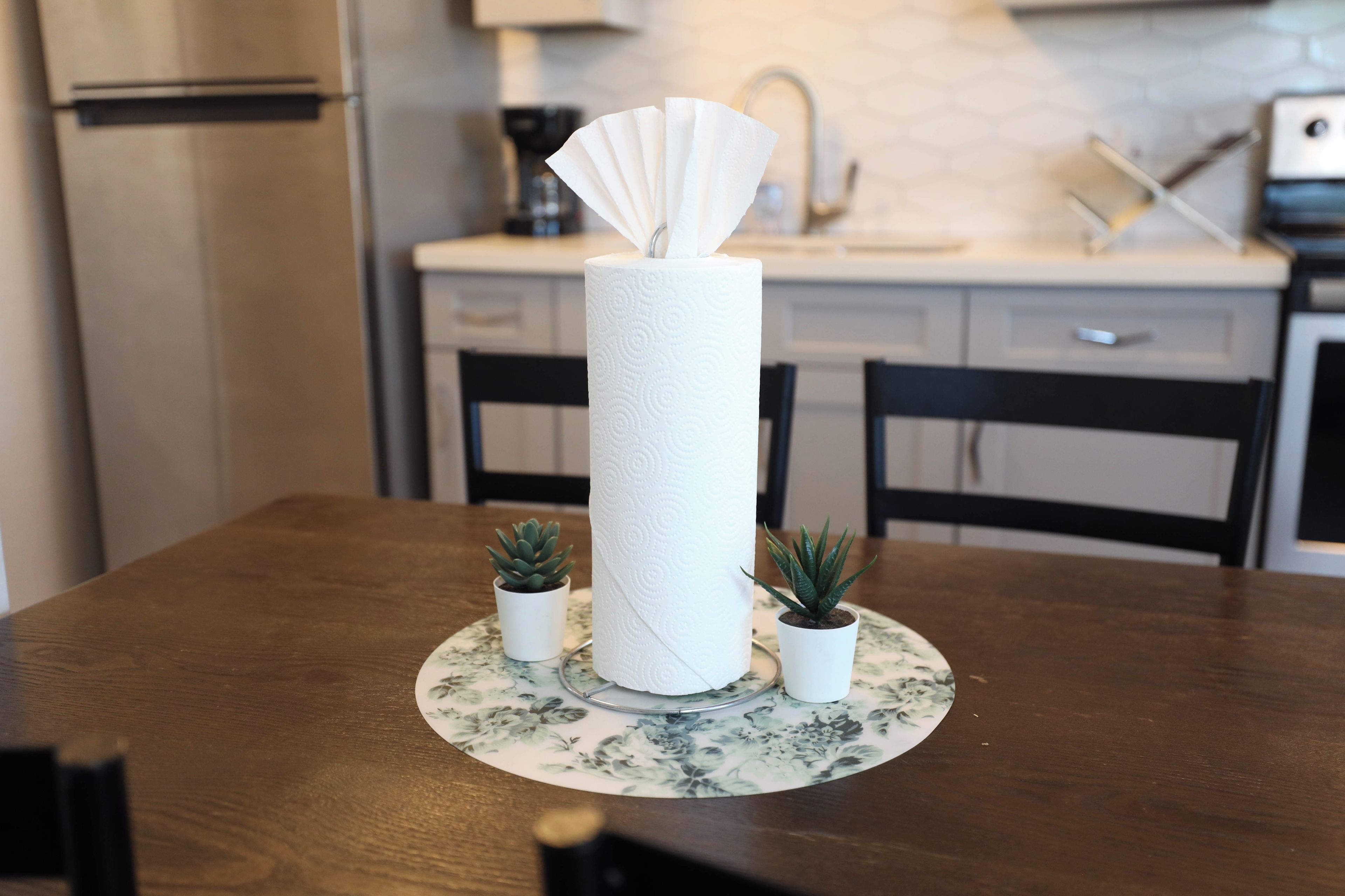 A dining table with a paper towel dispenser, two small potted plants, and a floral placemat.