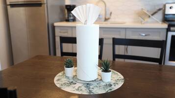 A dining table with a paper towel dispenser, two small potted plants, and a floral placemat.