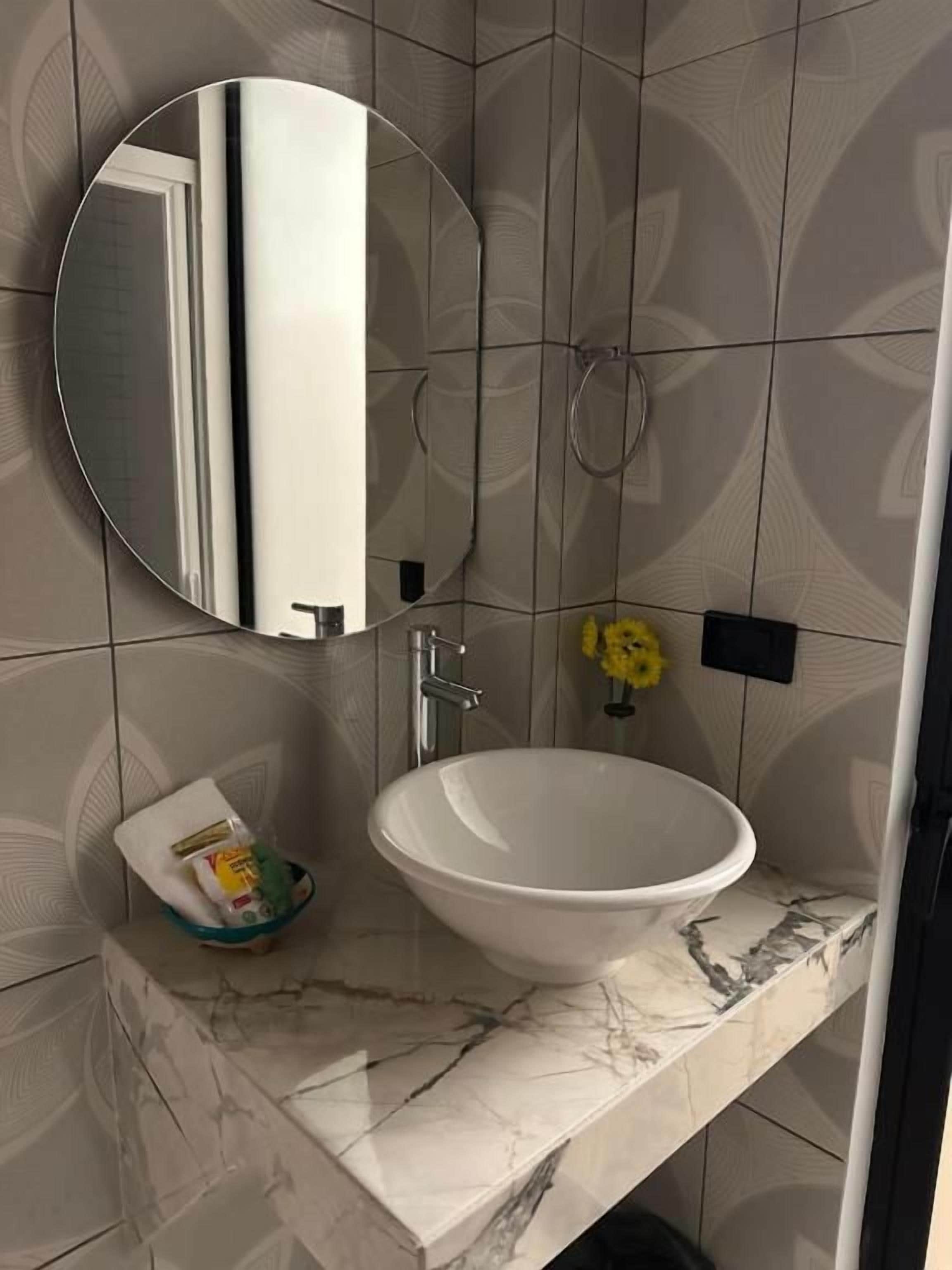 Ein Badezimmer mit einem runden Spiegel, einem weißen Waschbecken und einem Handtuchspender.