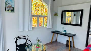 Een kamer met een glazen tafel, twee stoelen, een bureau, een spiegel en een raam met gordijnen.