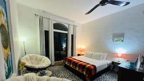 Een hotelkamer met een bed, een stoel, een bureau, een plafondventilator en uitzicht op het omliggende landschap.
