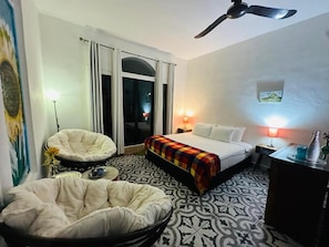 Een hotelkamer met een bed, een stoel, een bureau, een plafondventilator en uitzicht op het omliggende landschap.