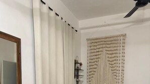 A bedroom with a bed, a bedside table, a chair, a window with curtains, a wall-mounted shelf, and a ceiling fan. - The Quetzal Cancun (Cancún)