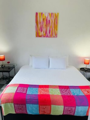 A hotel room with a bed, two bedside tables, a colorful quilt, and a piece of abstract art on the wall. - The Quetzal Cancun (Cancún)