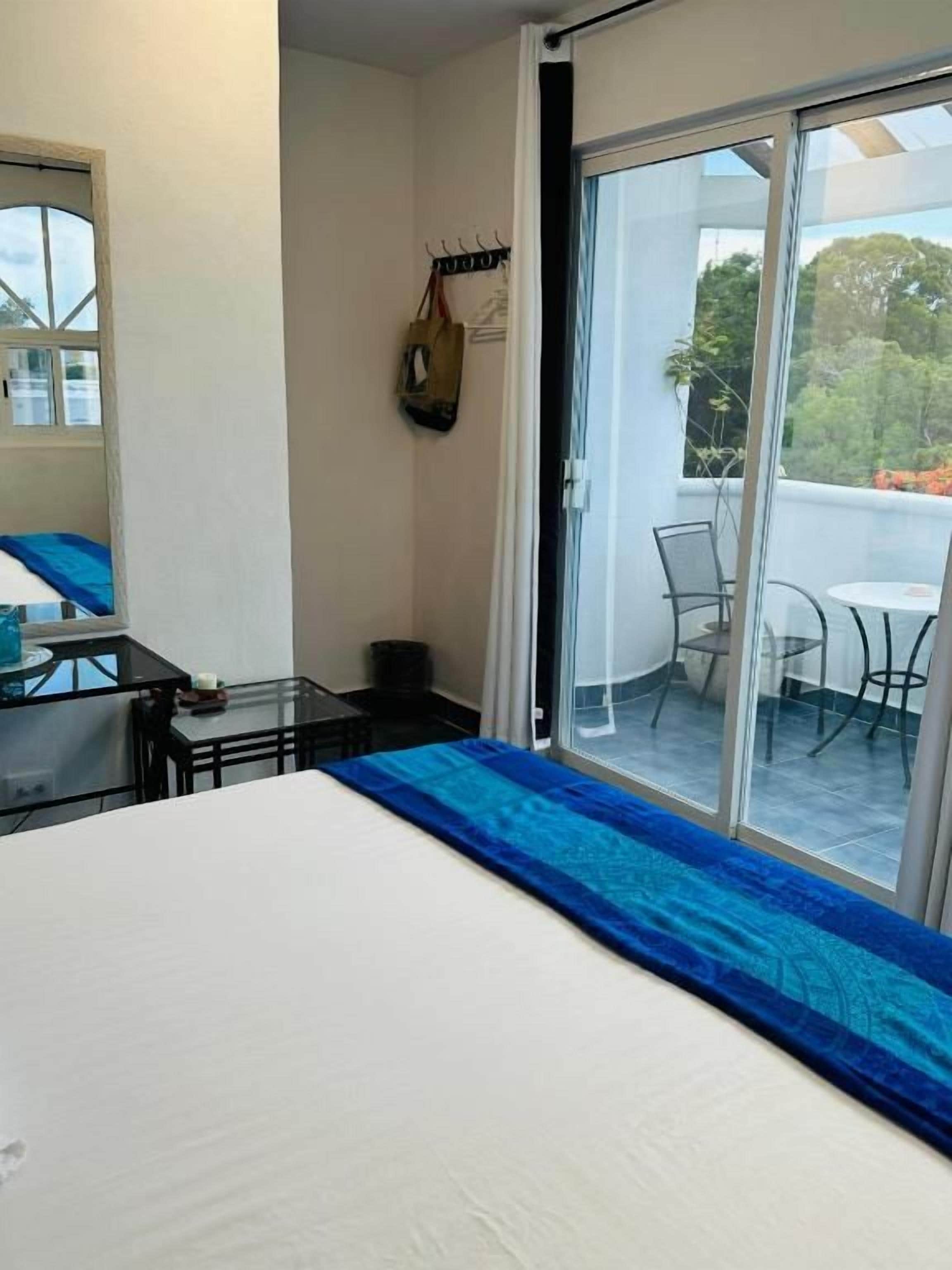 A hotel room with a bed, a small table, a chair, and a balcony with a view.