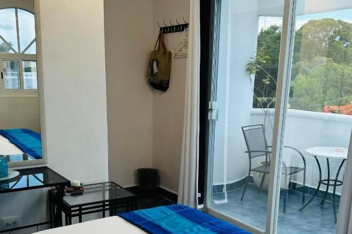 Een hotelkamer met een bed, een tafeltje, een stoel en een balkon met uitzicht.