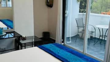 A hotel room with a bed, a small table, a chair, and a balcony with a view.