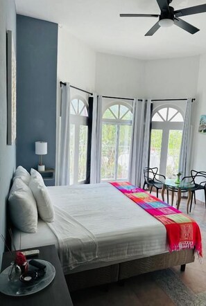 Un dormitorio con cama, mesita de noche, silla y ventana con cortinas.