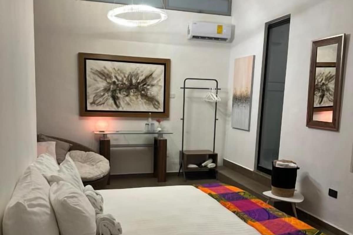 Een hotelkamer met een bed, nachtkastje, stoel, hanglamp en kunstwerken aan de muur.