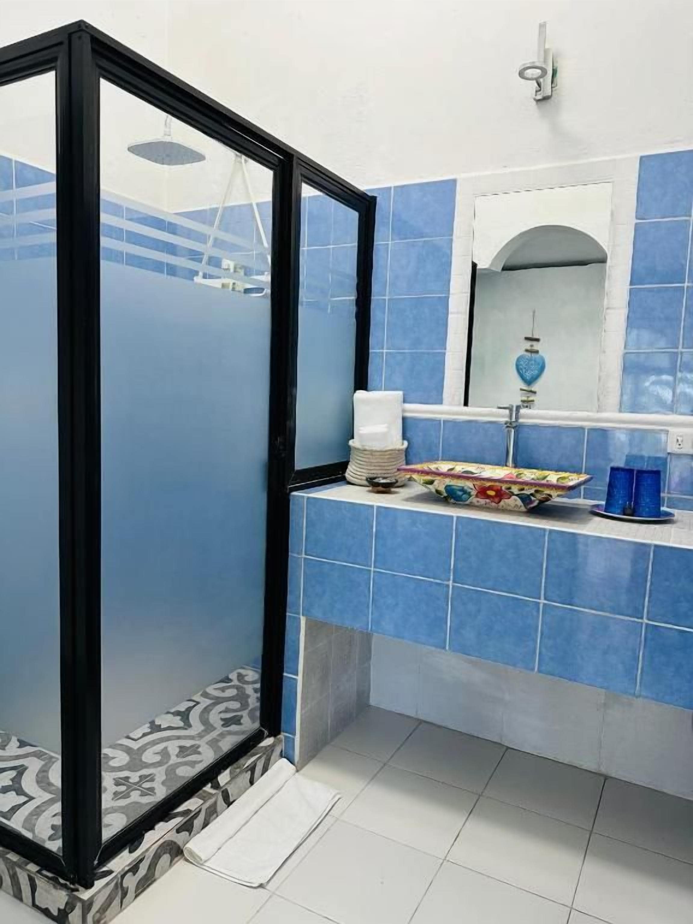 A bathroom with a glass partition, a sink with a mirror, and a towel rack.