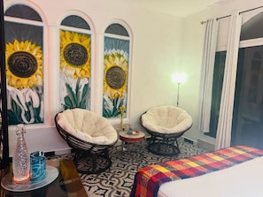 Una habitación de hotel con una cama, dos sillones, una mesita y tres cuadros de girasoles en las paredes.