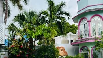 A swimming pool with a white deck, surrounded by tropical plants and a multi-story building with pink accents.