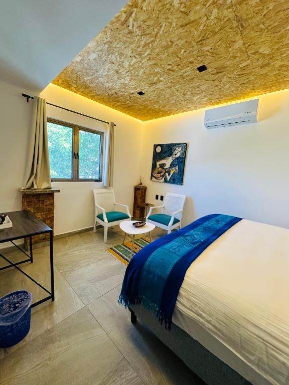 A bedroom with a bed, a desk, two chairs, a window, and a painting on the wall.