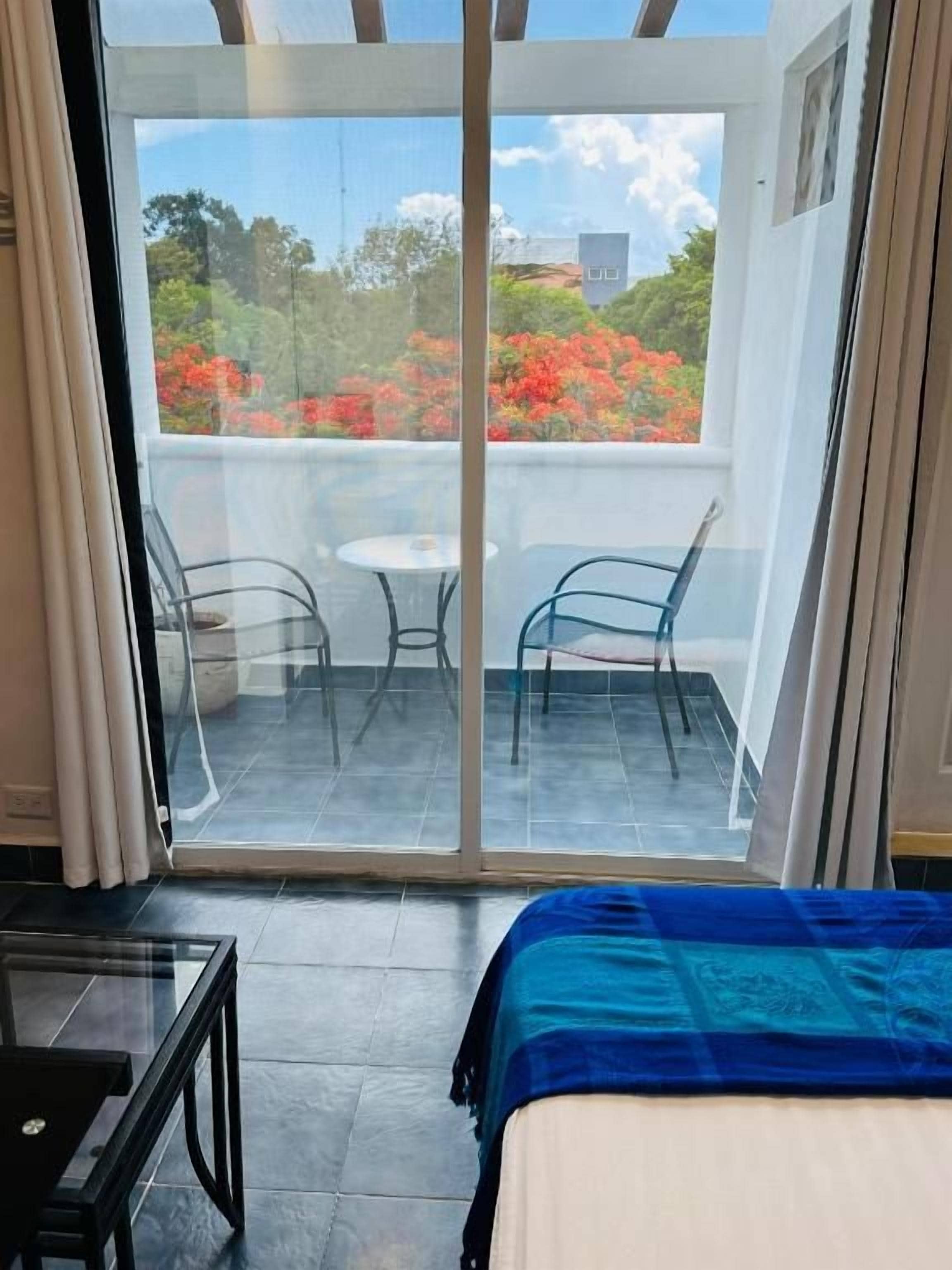 Ein Zimmer mit einem Bett, einer Glastür zu einem Außenbereich mit Tisch und Stühlen sowie Blick auf Bäume und Blumen.