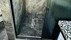 Een douchecabine met glazen wanden, een handdouche, een klein raam en een betegelde vloer.