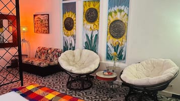 A room with a bed, two armchairs, a patterned rug, and a wall with three sunflowers.