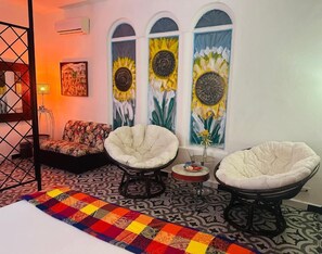 A room with a bed, two armchairs, a patterned rug, and a wall with three sunflowers.