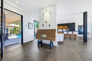 A modern interior with a wooden bench, a kitchen area, and a view of an outdoor pool. - Soledad Sky House | Pool + Sweeping Ocean Views (San Diego)