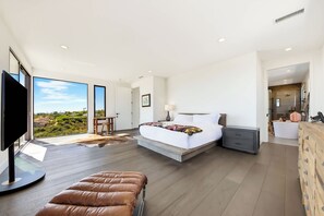 A modern bedroom with a large bed, a TV, and a view of the outdoors. - Soledad Sky House | Pool + Sweeping Ocean Views (San Diego)